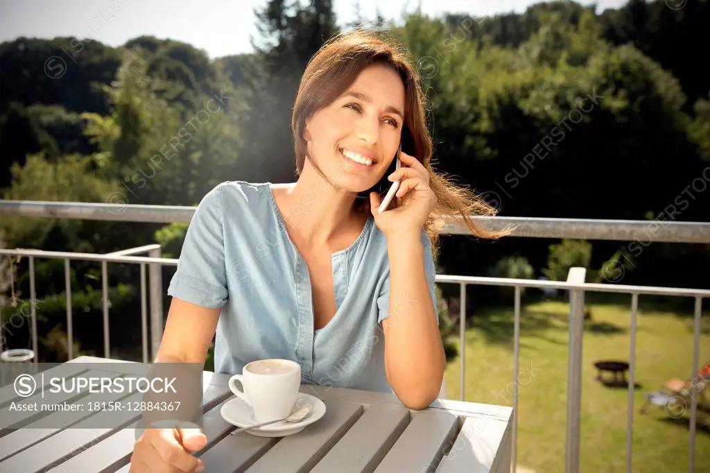Woman on balcony with cup of coffee on the phone