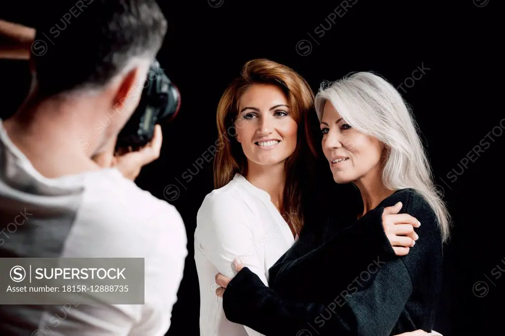 Man photographing two women in front of black background