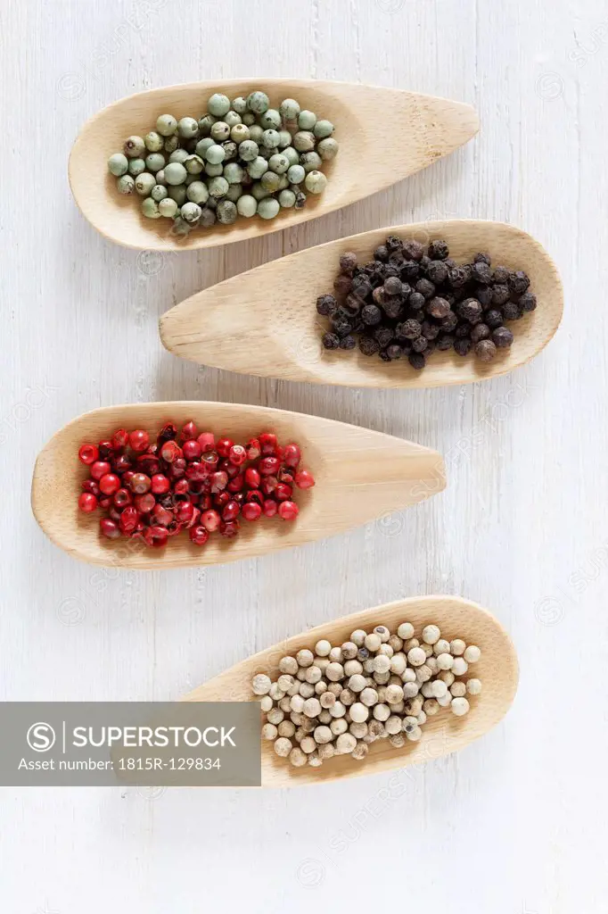 Variety of peppercorns on wooden spoon, close up