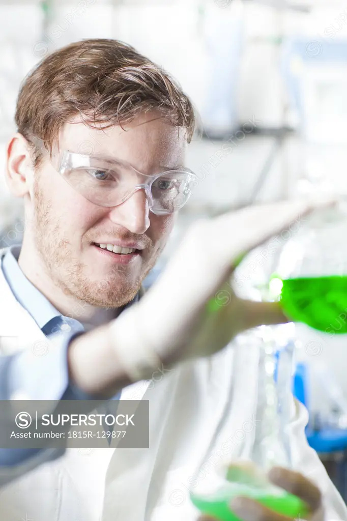 Germany, Young scientist pouring green liquid into erlenmeyer flask