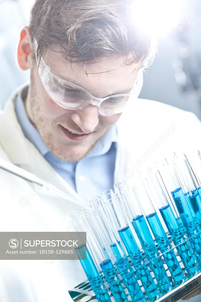 Germany, Young scientist pipetting blue liquid into test tubes, close up