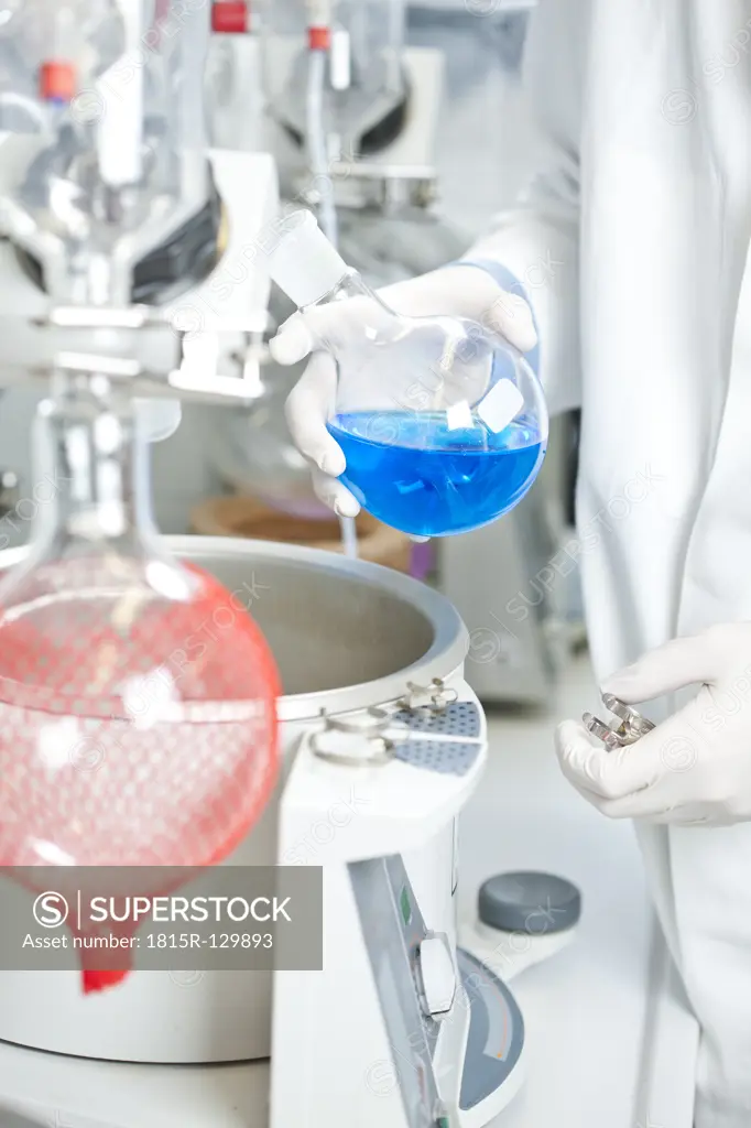 Germany, Young scientist examining blue liquid on rotary evaporator