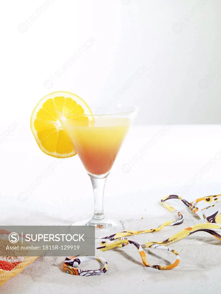 Orange juice cocktail on sand against white background