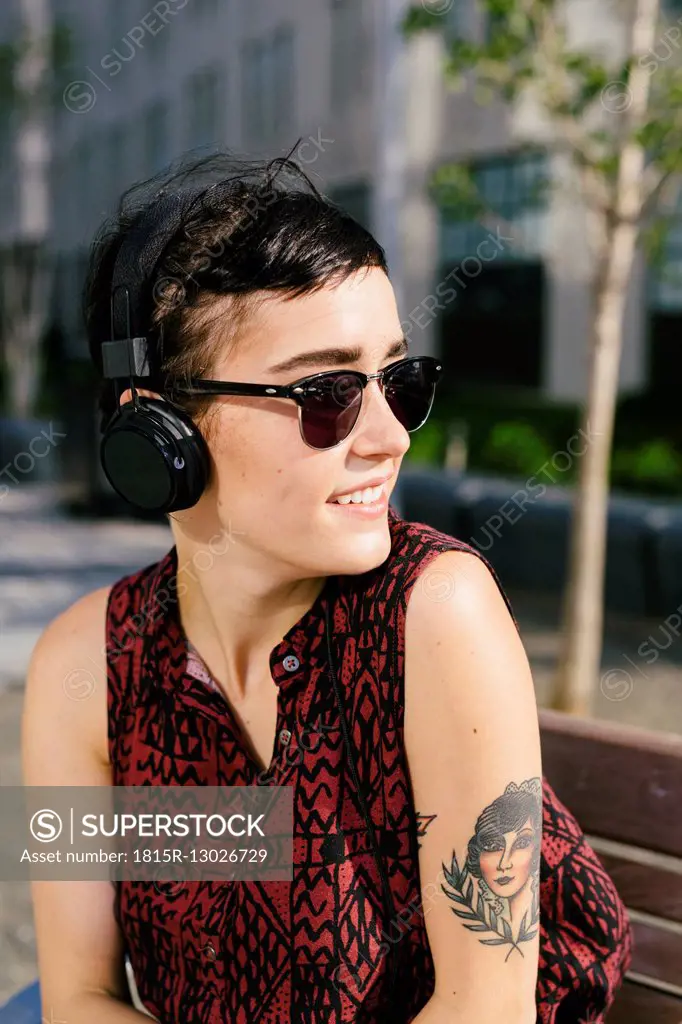 Portrait of tattooed young woman with headphones and sunglasses
