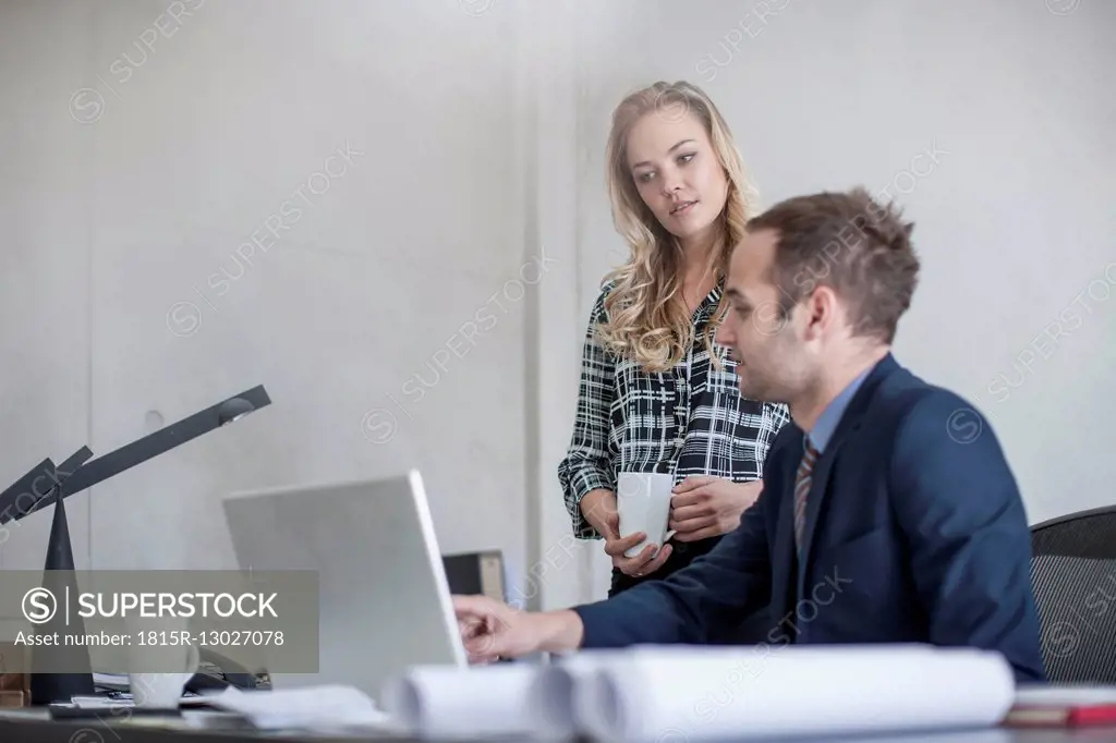 Businessman at desk with colleague looking at laptop