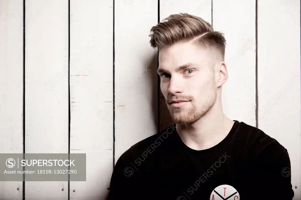 Portrait of young man with quiff in front of wooden wall