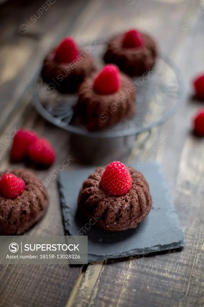 Mini cakes with raspberries on cooling grid and slate, wood