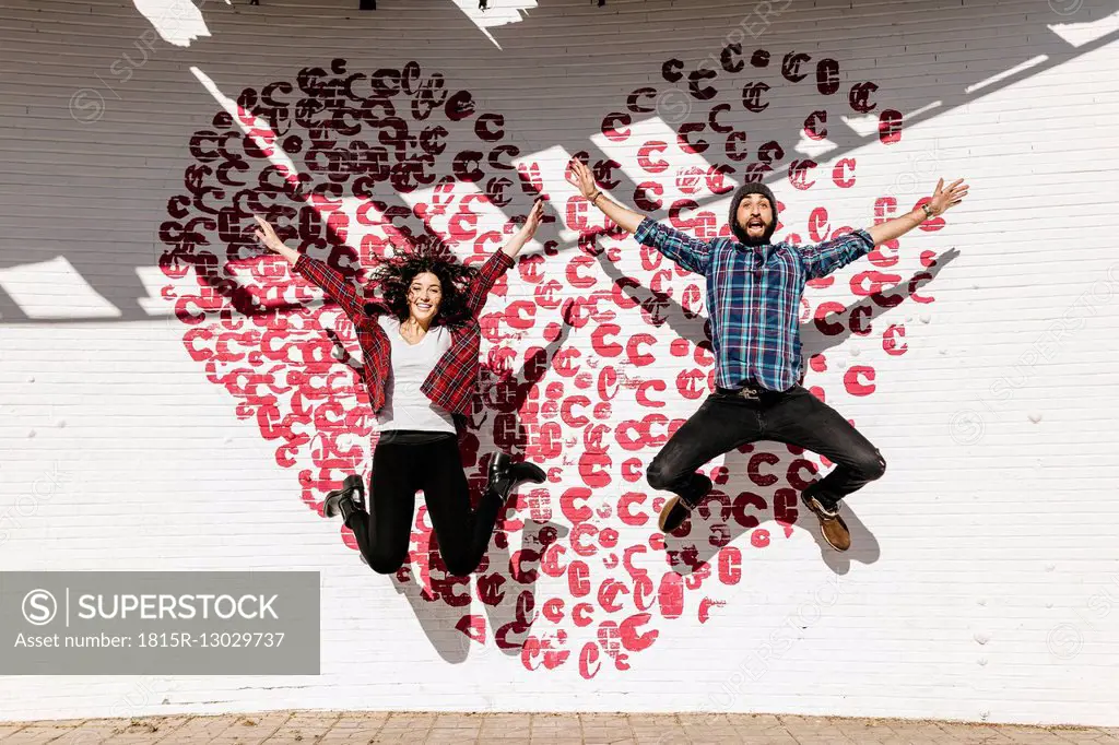 Happy young couple jumping in front of a brick wall with a heart
