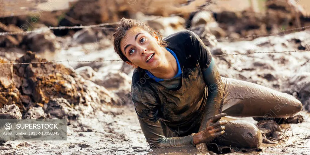 Participant in extreme obstacle race crawling under barbed wire