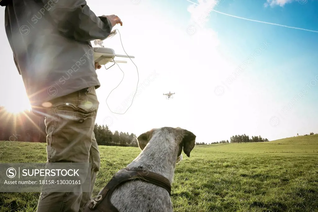 Man on a meadow flying drone while his dog watching
