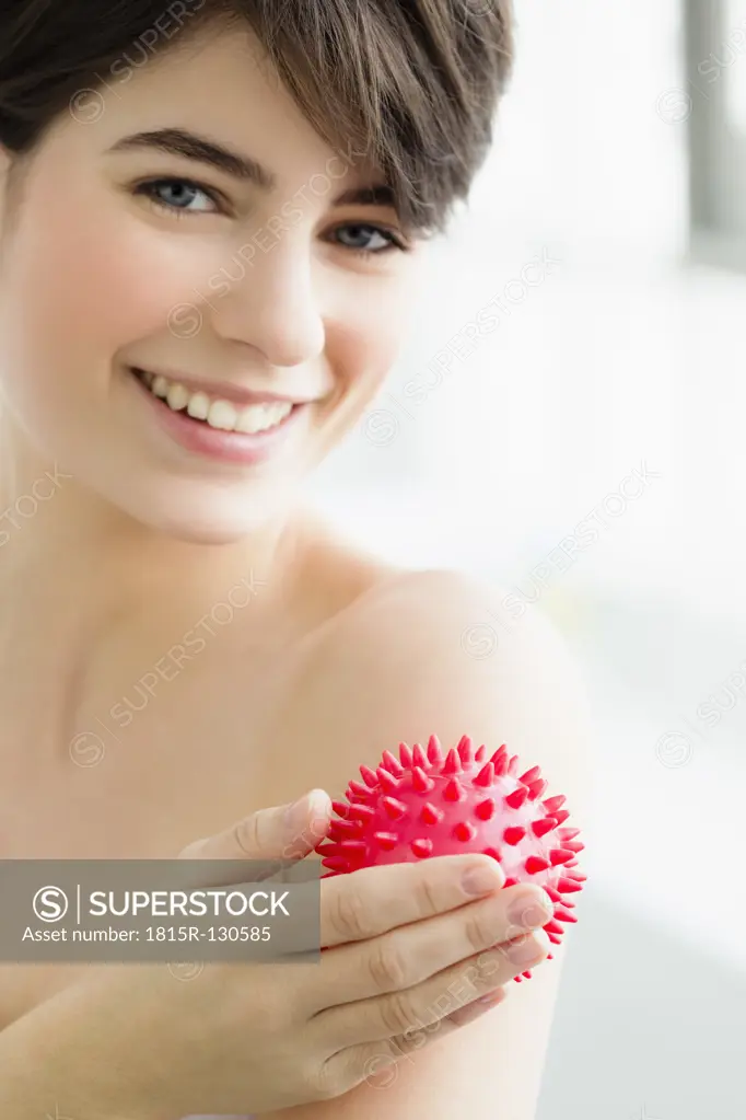 Germany, Bavaria, Munich, Young woman massaging with massage ball, smiling