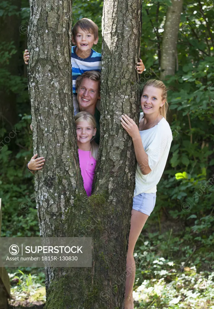 Austria, Portrait of friends standing behind tree trunk, smiling
