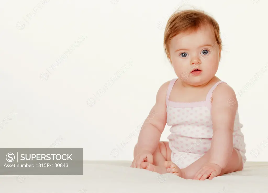 Portrait of baby girl sitting on bed, close up