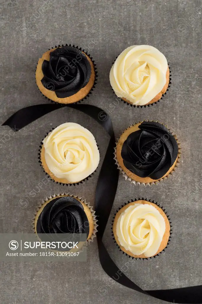 Six cup cakes with black and cream coloured buttercream topping and black ribbon