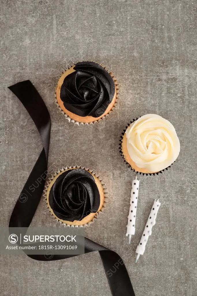 Cup cakes with black and cream coloured buttercream topping, ribbon and two candles