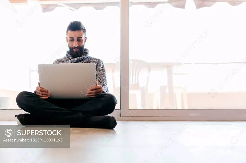 Bearded young man working at home relaxed, sitting on the floor, using laptop