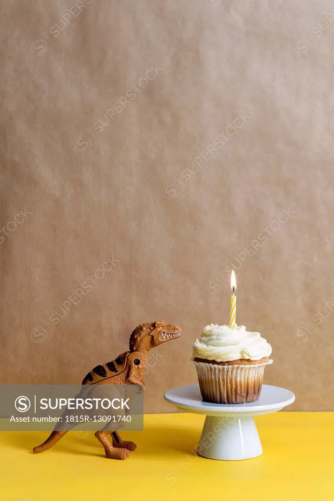 Toy dinosaur and cup cake with lighted candle on a cake stand