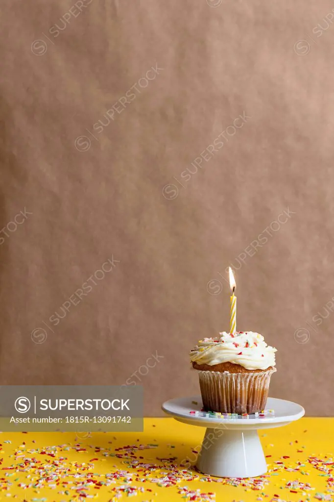 Cup cake with lighted candle sprinkled with sugar granules on a cake stand