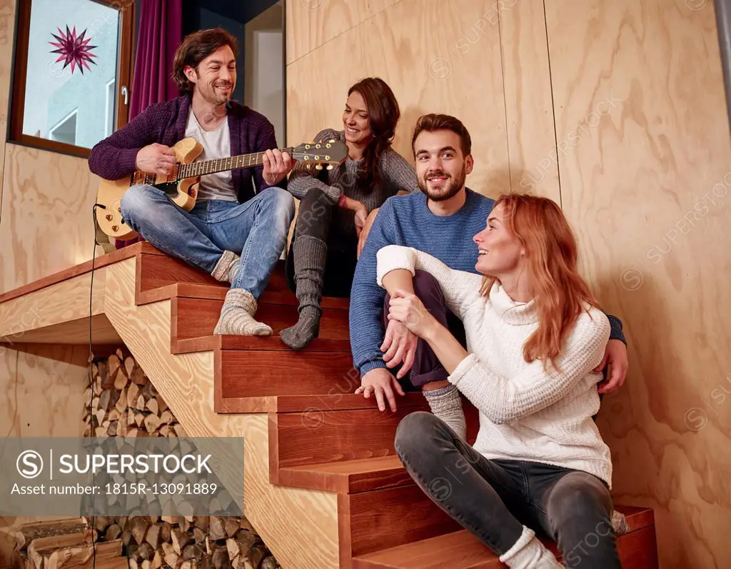 Friends sitting on wooden stairs playing guitar