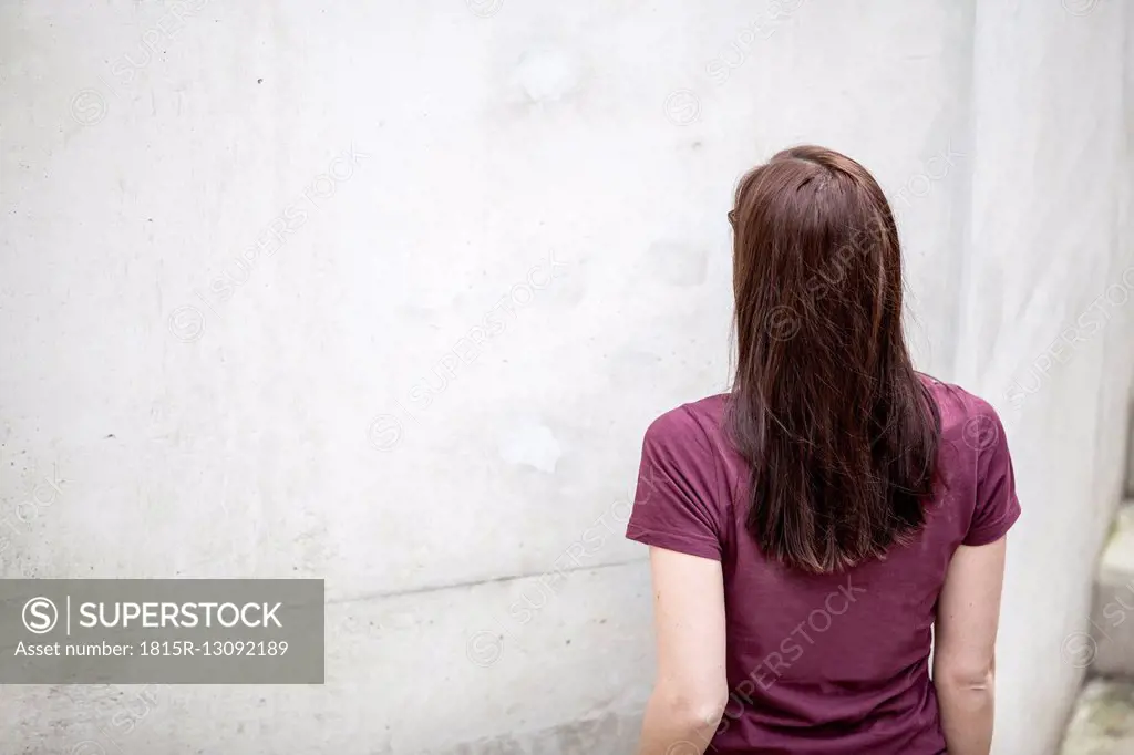Back view of young woman standing in front of concrete wall