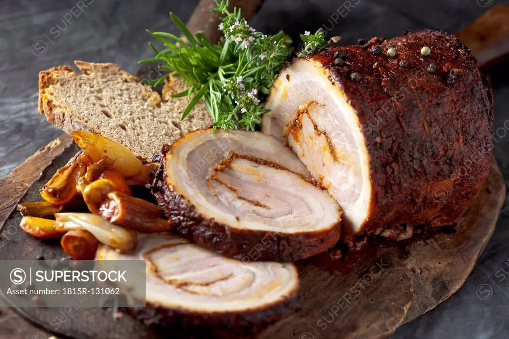 Rolled roast pork and braised vegetables on wooden board, close up
