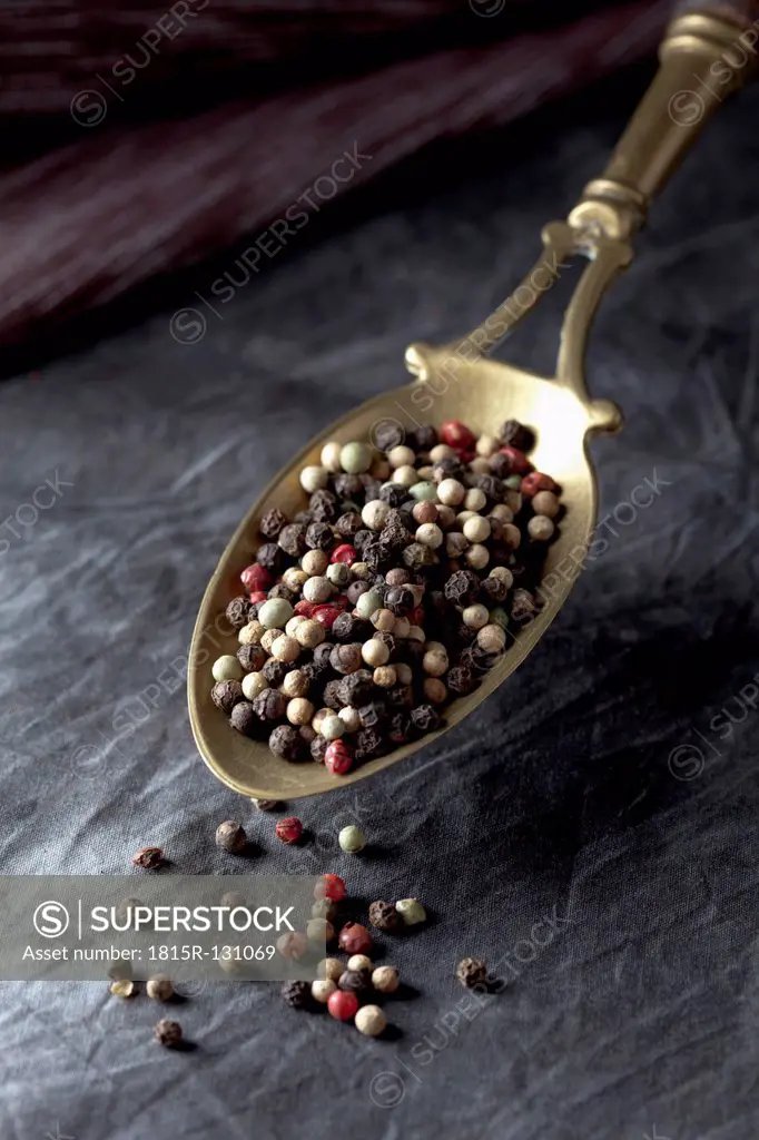 Brass spoon with peppercorns on textile,close up