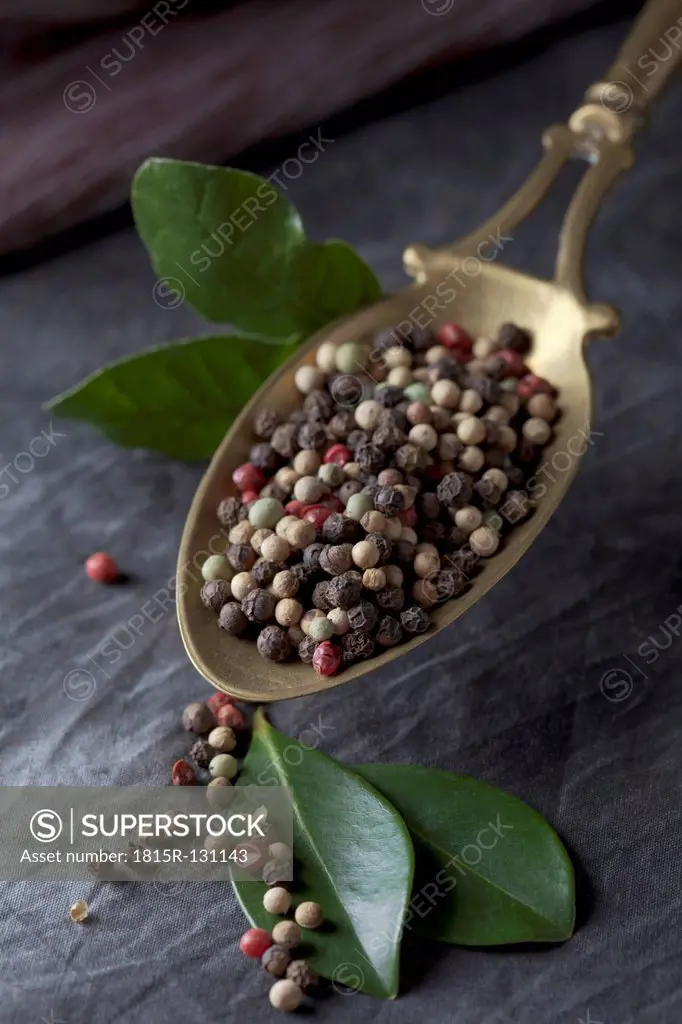 Brass spoon with peppercorns and leaves on textile, close up