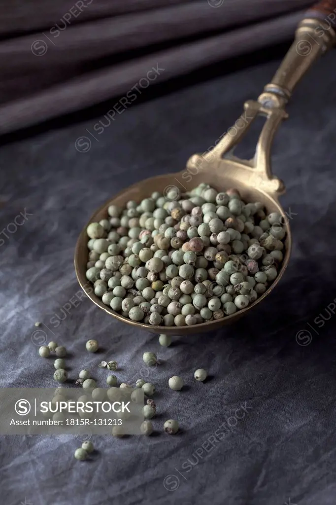 Brass spoon with green peppercorns on textile, close up