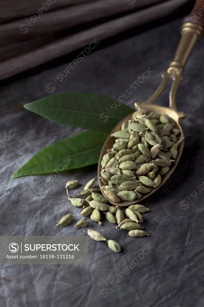 Brass spoon with cardamom seeds and leaves on textile, close up