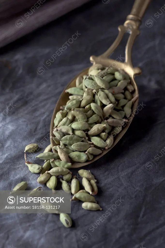 Brass spoon with cardamom seeds on textile, close up
