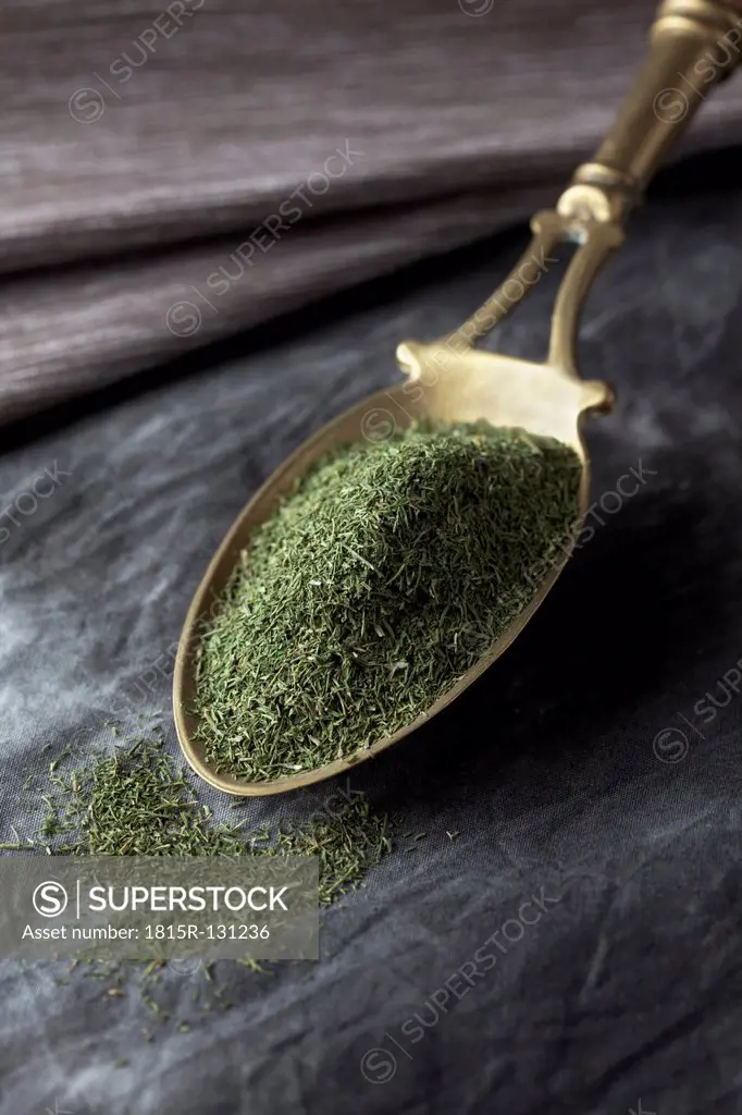 Brass spoon with dill on textile, close up