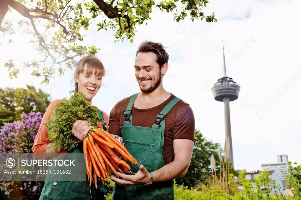 Germany, Cologne, Young couple holding bunch of carrots, smiling