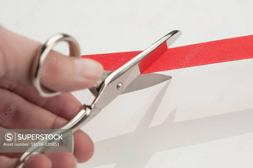 Human hand cutting inauguration red ribbon, close-up