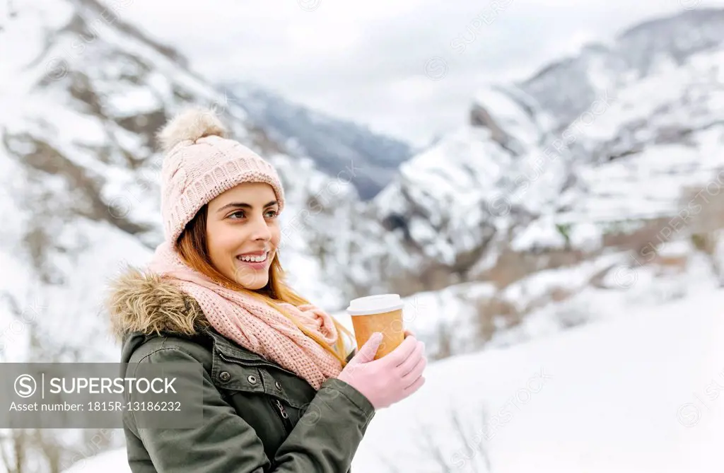 Spain, Asturias, happy young woman with coffee to go in the snowy mountains