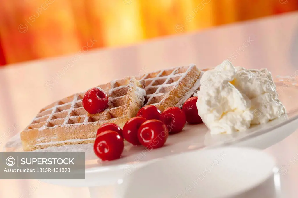 Plate of wafers with icing sugar, whipped cream and cherries, close up