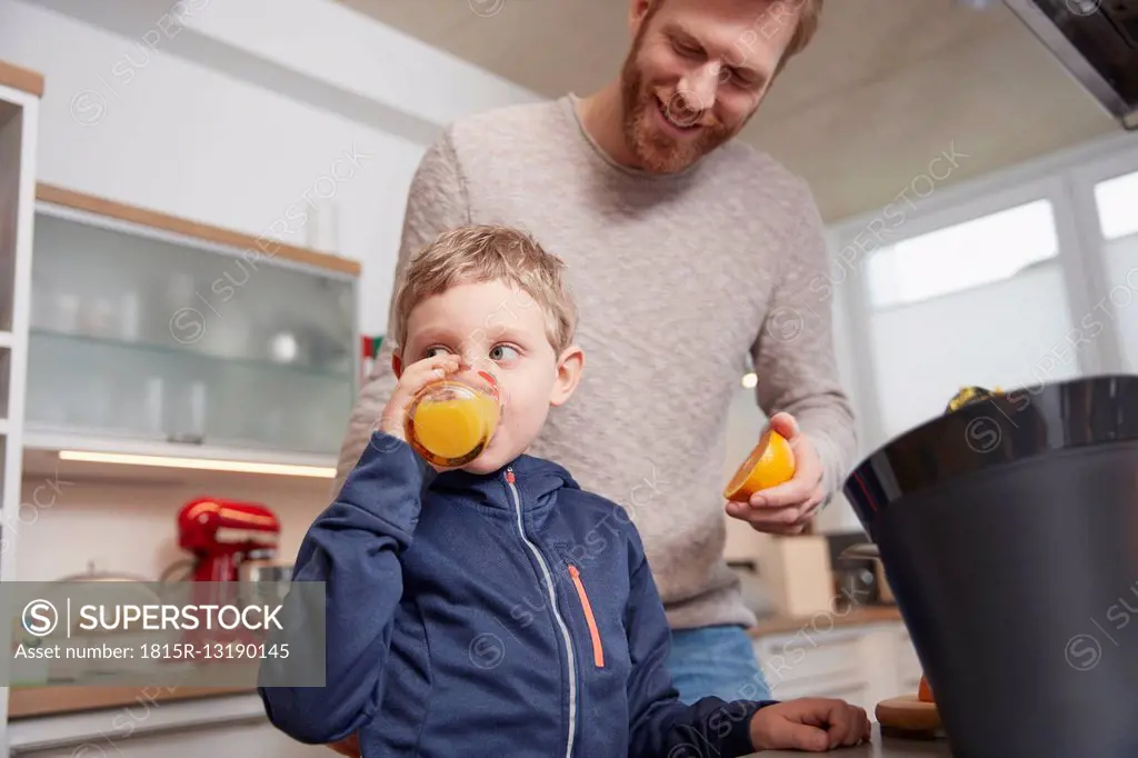Father with son drinking feshly squeezed orange juice in kitchen