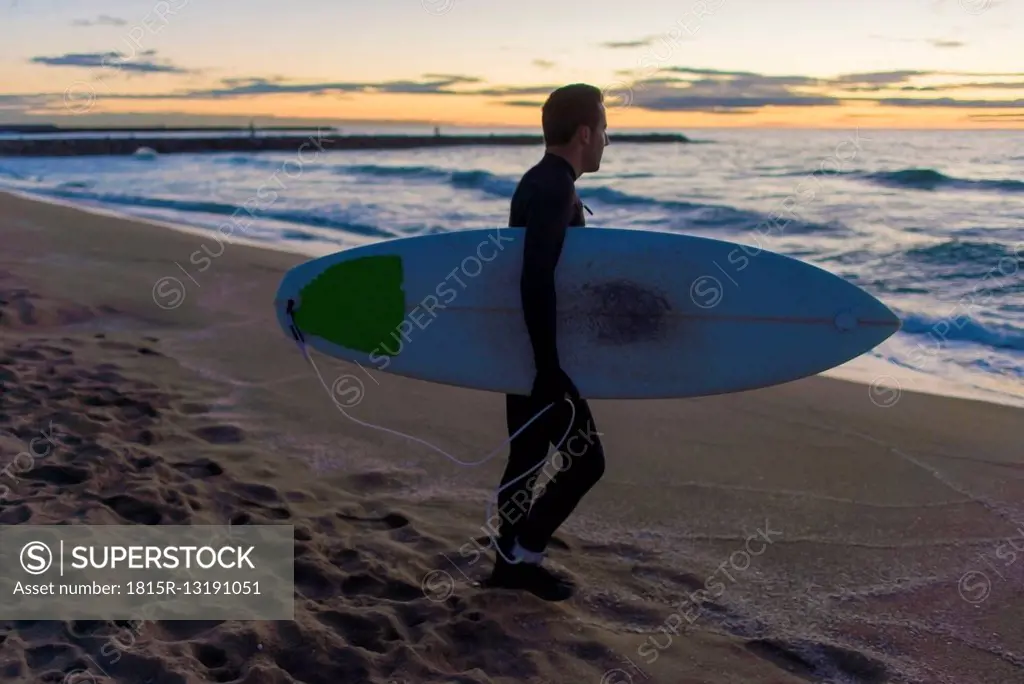 Surfer with his board on the beach at sunrise