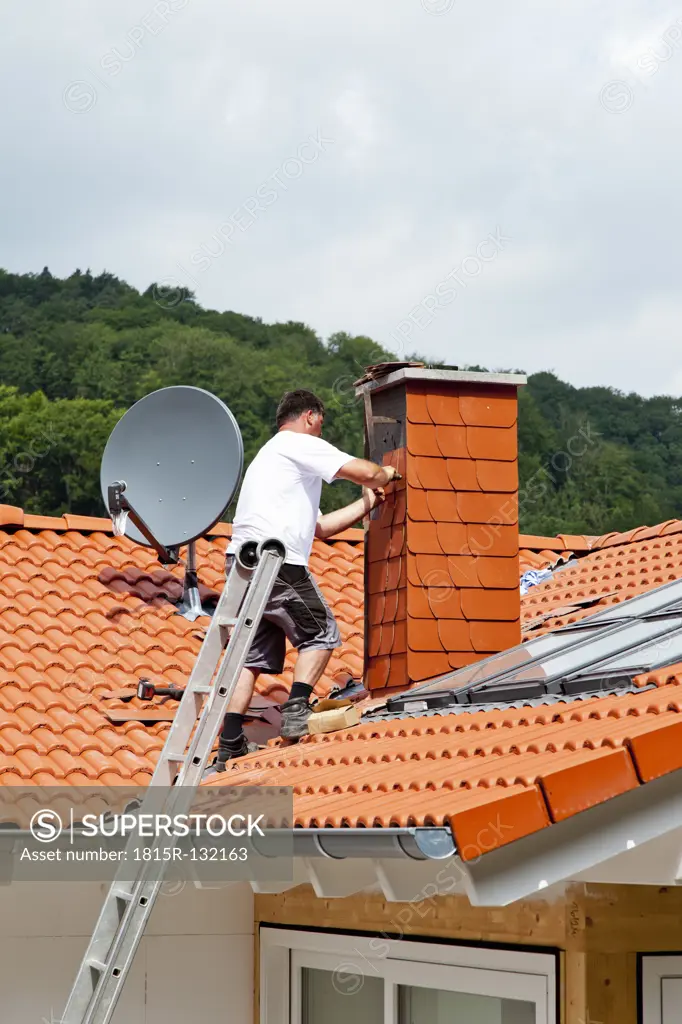 Europe, Germany, Rhineland Palatinate, Man covering chimney with roofing shingles