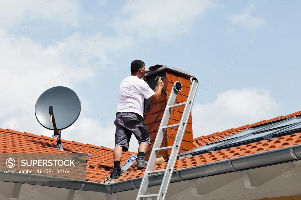 Europe, Germany, Rhineland Palatinate, Man covering chimney with roofing shingles