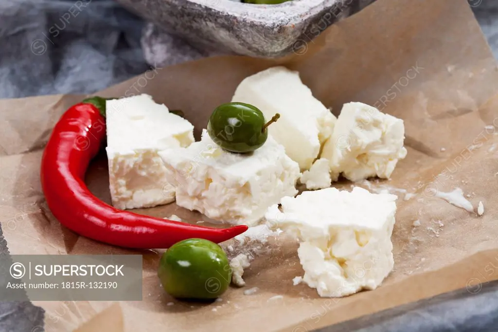 Sheep's cheese with green olives in olive oil and chili on brown paper, close up