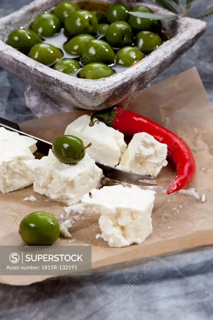 Bowl of green olives in olive oil with sheep's cheese and chili on textile, close up