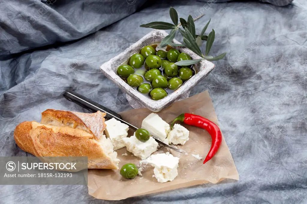Sheep's cheese with green olives in olive oil, chili and white bread on textile, close up