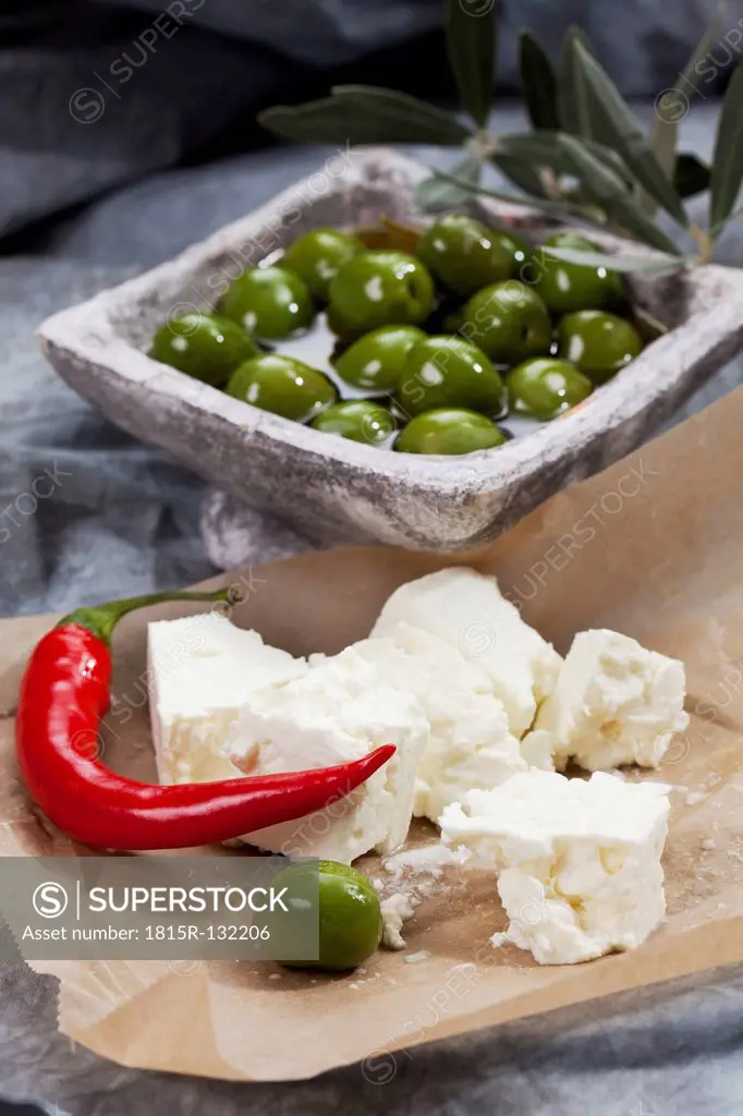 Bowl of green olives in olive oil with sheep's cheese and chili on textile, close up