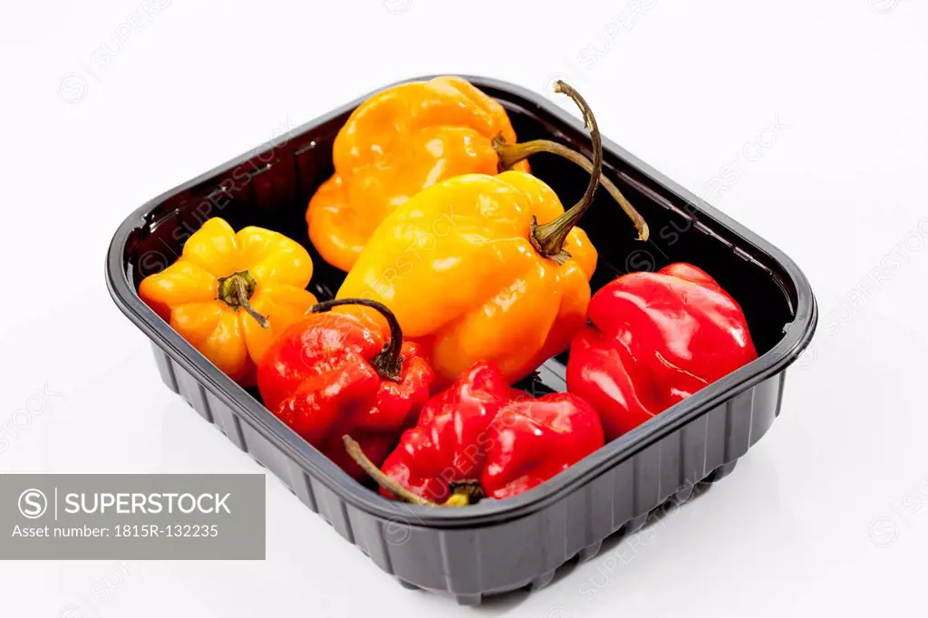 Plastic box with habaneros peppers on white background