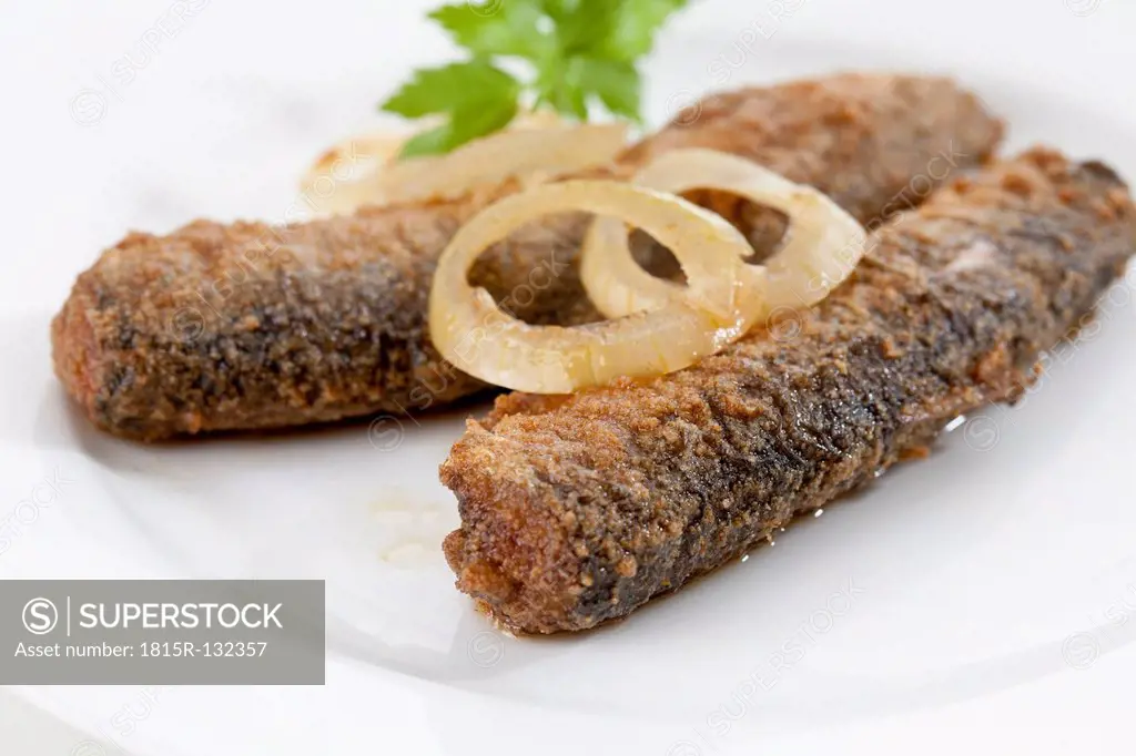 Fried herring with onions and vinegar on plate, close up