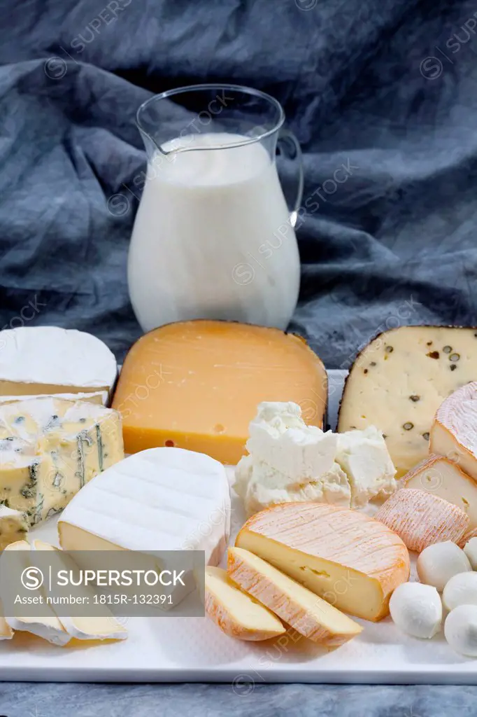 Varieties of cheeses on chopping board with carafe of milk on textile