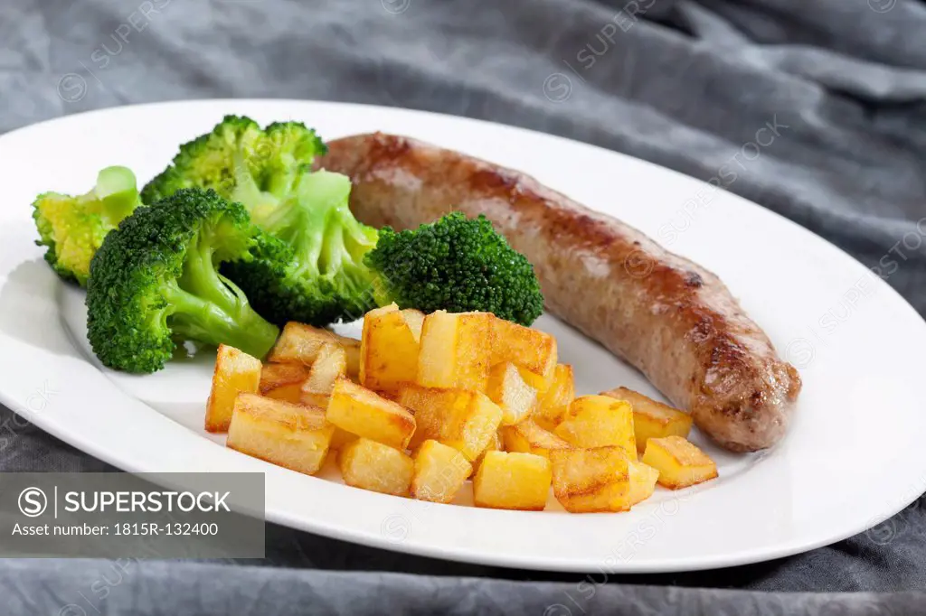 Grilling sausage with roasted potatoes and broccoli on plate, close up