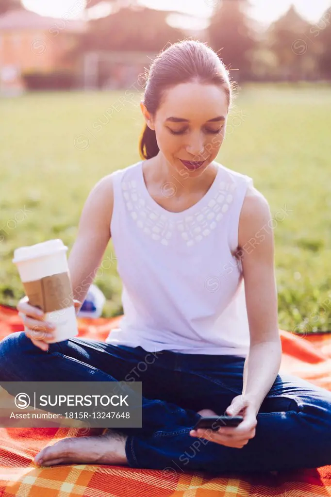Student at the park having a coffee to go, looking on smartphone