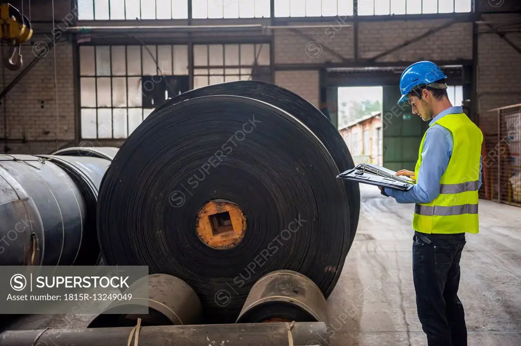 Worker with documents in factory hall with rolls of rubber