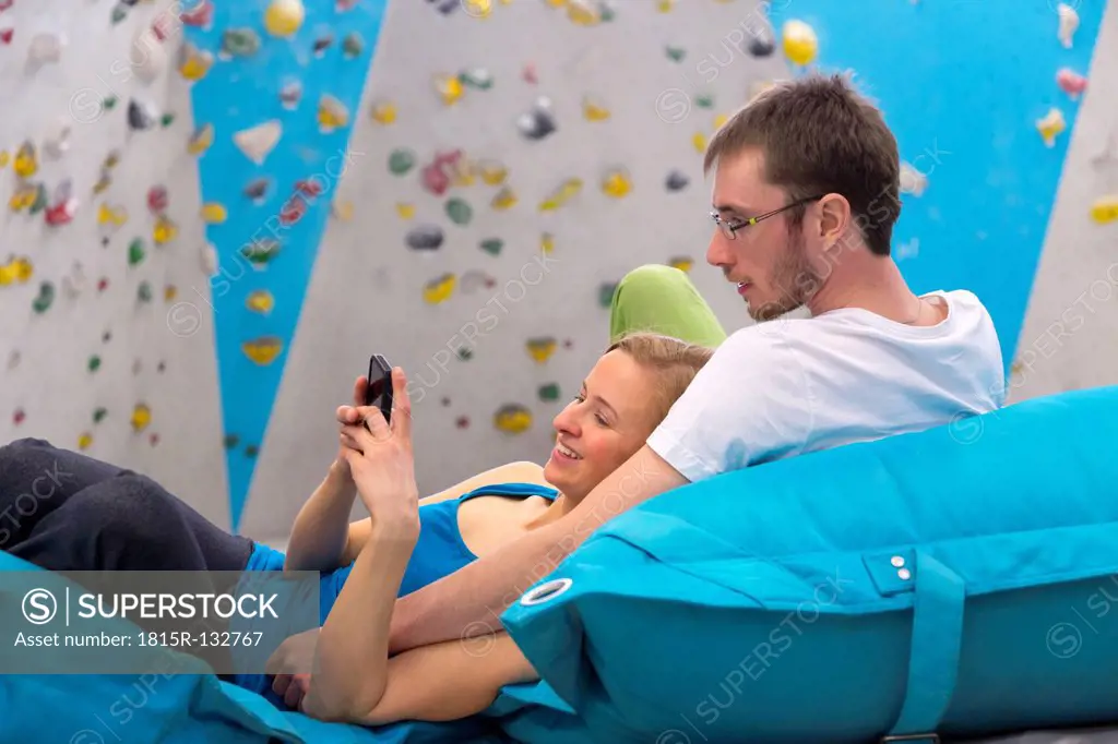 Germany, Bavaria, Munich, Young couple relaxing and using mobile phone, smiling